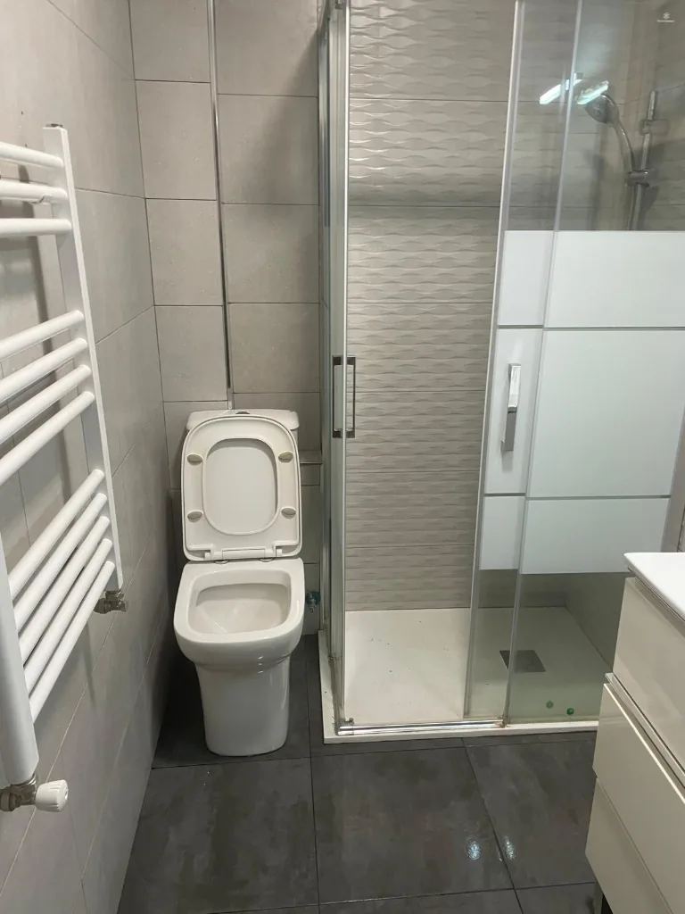 Baño reformado con plato de ducha, mampara corredera y radiador toallero